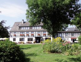 Außenansicht eines traditionellen Fachwerkhauses mit Garten und Bäumen.