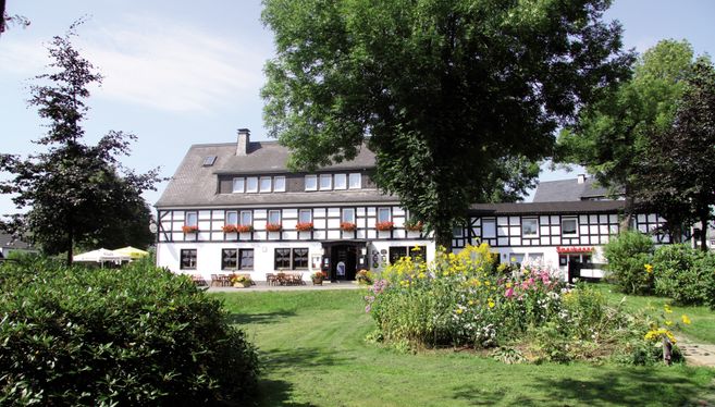Außenansicht eines traditionellen Fachwerkhauses mit Garten und Bäumen.